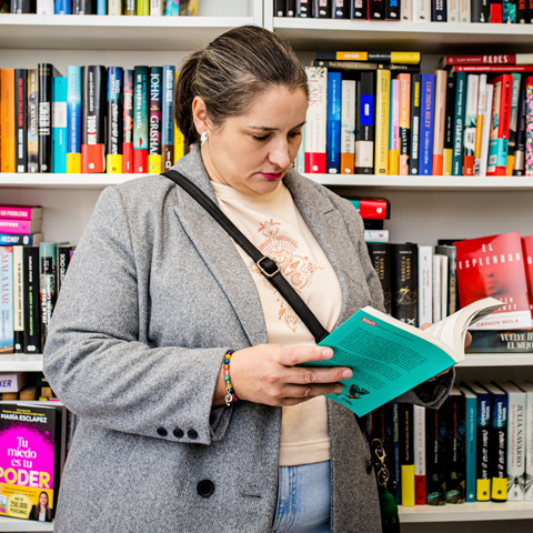 Clienta concentrada lee un libro turquesa frente a estanterías llenas de títulos en Librería Lilura, Lasarte-Oria, Buruntzaldea