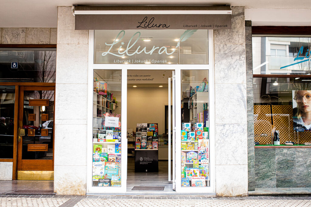 Fachada de Librería Lilura con puertas abiertas y escaparate repleto de libros y juegos de mesa en Lasarte-Oria, Buruntzaldea